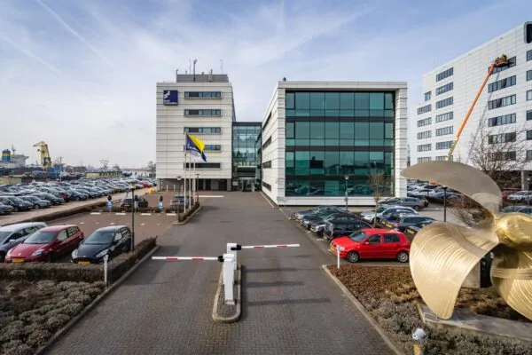 Kantoorgebouw van STC Group aan de Waalhaven in Rotterdam met parkeerterrein, vlaggenmast en grote scheepsschroef op de voorgrond.